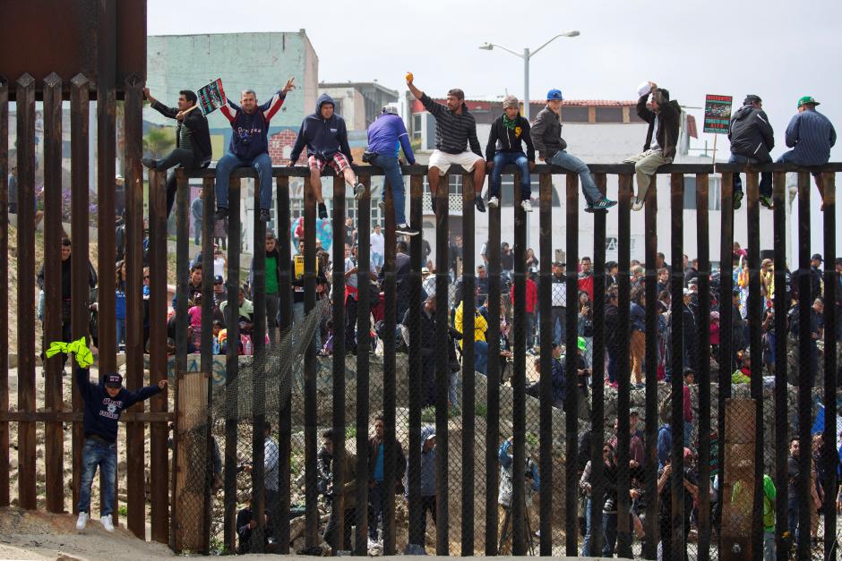People in Mexico climb the border wall fence as a caravan of migrants and supporters reached the United States-Mexico border near San Diego, California