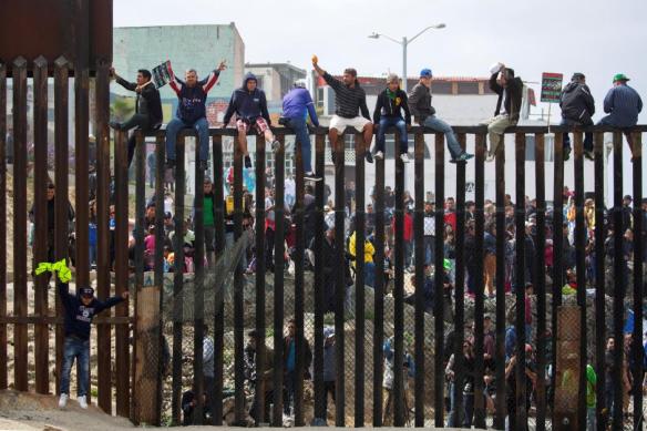 People in Mexico climb the border wall fence as a caravan of migrants and supporters reached the United States-Mexico border near San Diego, California